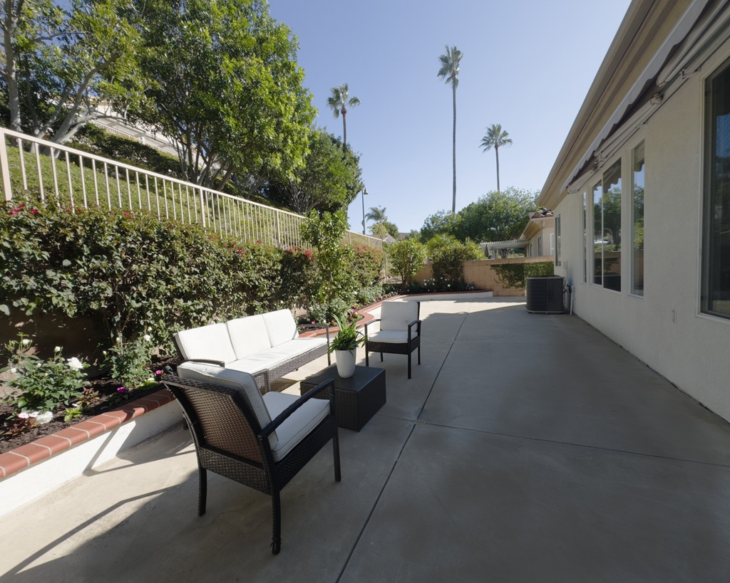 A patio with furniture and a white wall with numerous windows.