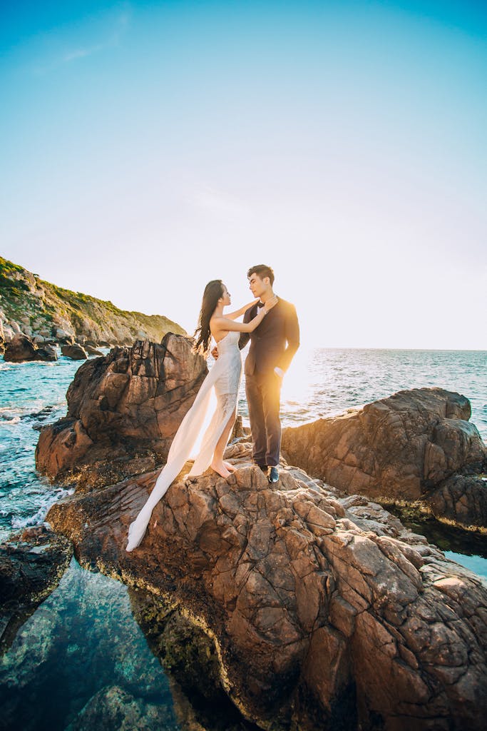 A couple posing on rocky seaside for a wedding photoshoot in Vietnam under a clear sunny sky.