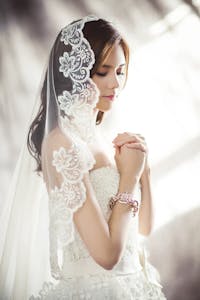 Beautiful bride in lace gown and veil, captured in soft lighting.