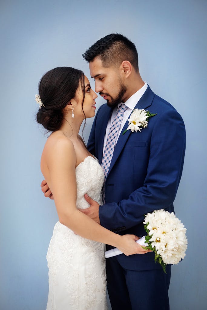 Bride and groom sharing a tender moment with bouquet against a blue background.