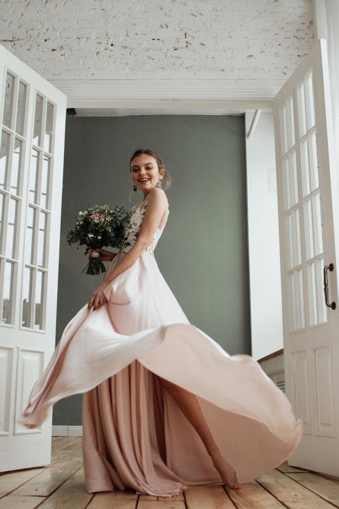 Joyful bride in an elegant gown twirling with bouquet in a bright indoor space.