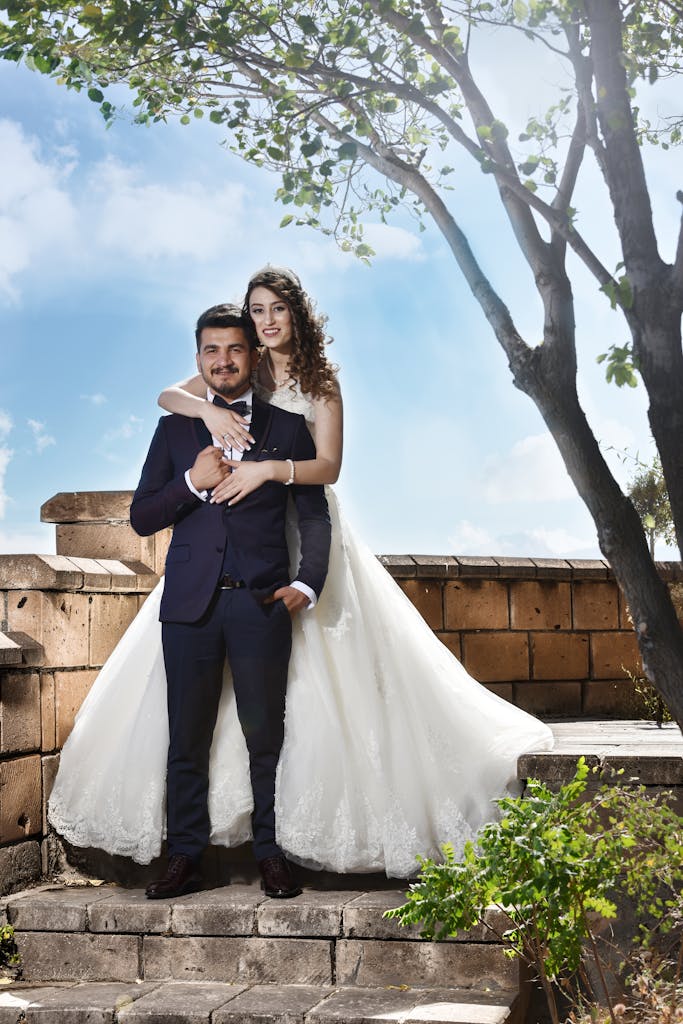 Romantic outdoor wedding photo of a happy couple embracing under a tree.